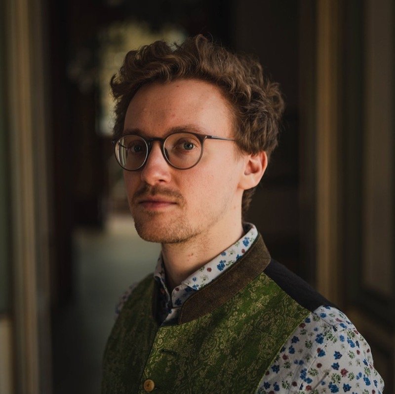 Porträt von Leonhard Waltersdorfer mit Brille und grüner Weste im Palais Auersperg.