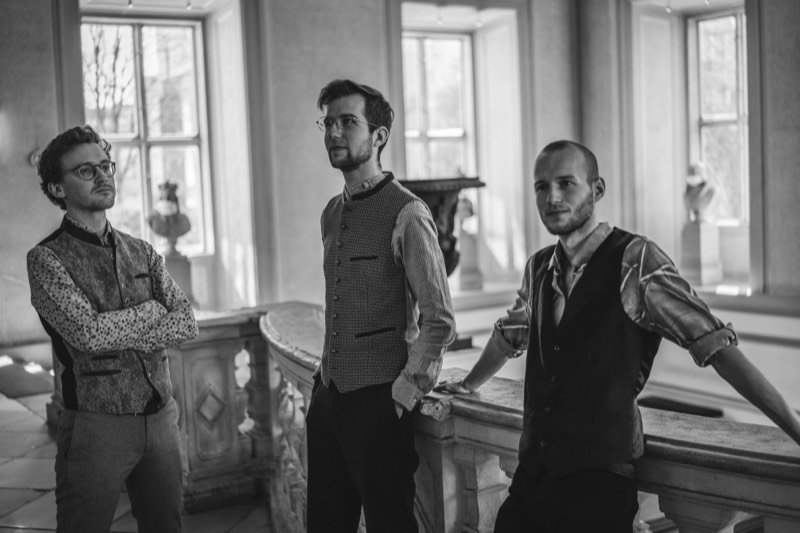 Schwarzweiß: die drei Musiker lehnen an einer Balustrade.